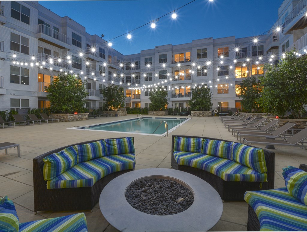Pool at night with overhead string lights and soft seating around fire pit