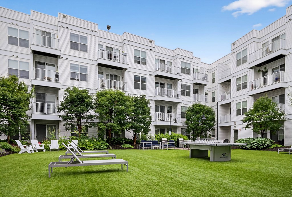 A sunny day at a white apartment complex with a green lawn and a table and chairs set up.