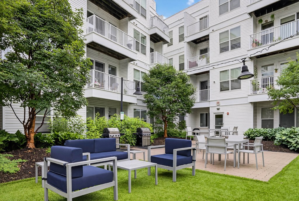 A white apartment building with blue chairs and tables in front.