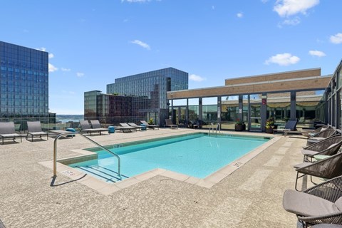 A swimming pool surrounded by lounge chairs and buildings in the background.