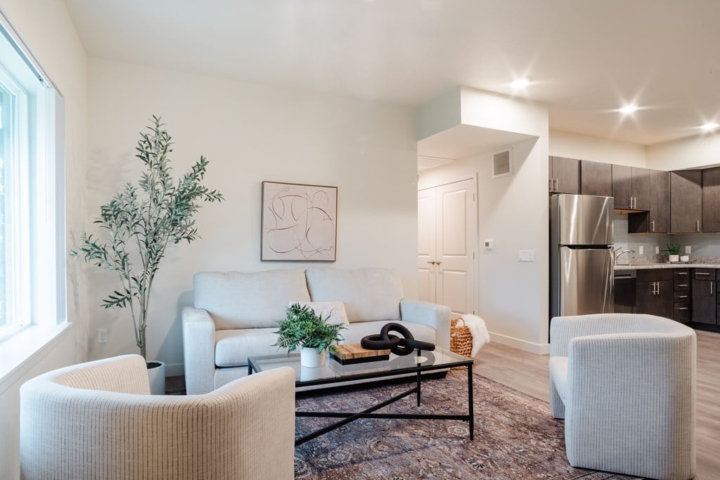 A living room with a white couch, a white chair, a black coffee table, and a plant.
