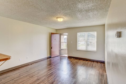 the living room and dining room of an empty house with wood floors and a door