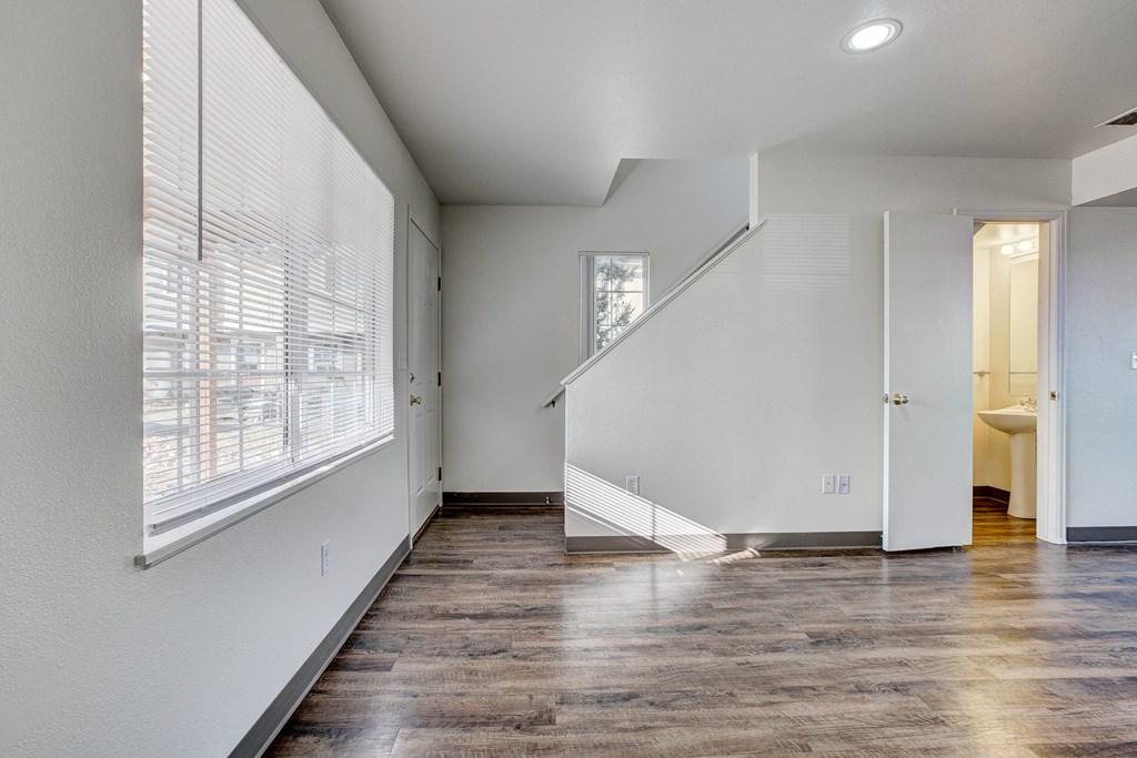 A spacious room with wooden floors and a staircase leading to another room.