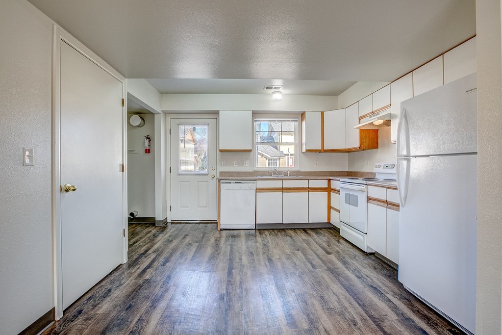 A kitchen with white appliances and wooden floors.
