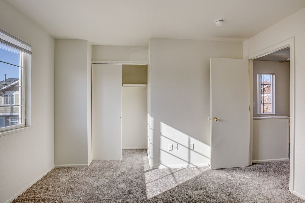 A room with white walls and carpeted floor with a window on the left.