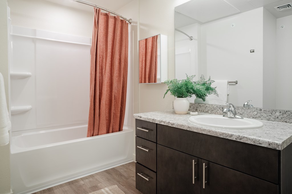 A bathroom with a white tub, sink, and brown cabinets.