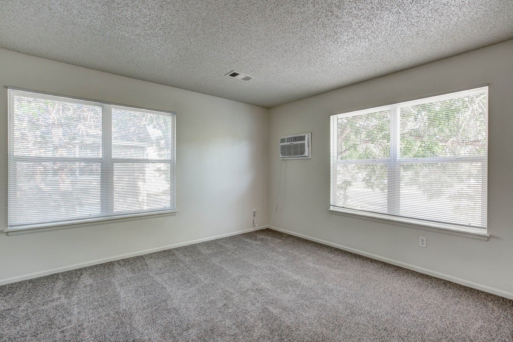 an empty living room with two windows and carpeting