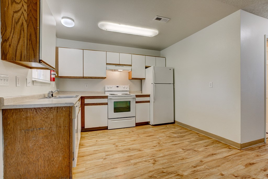 an empty kitchen with white appliances and wood flooring