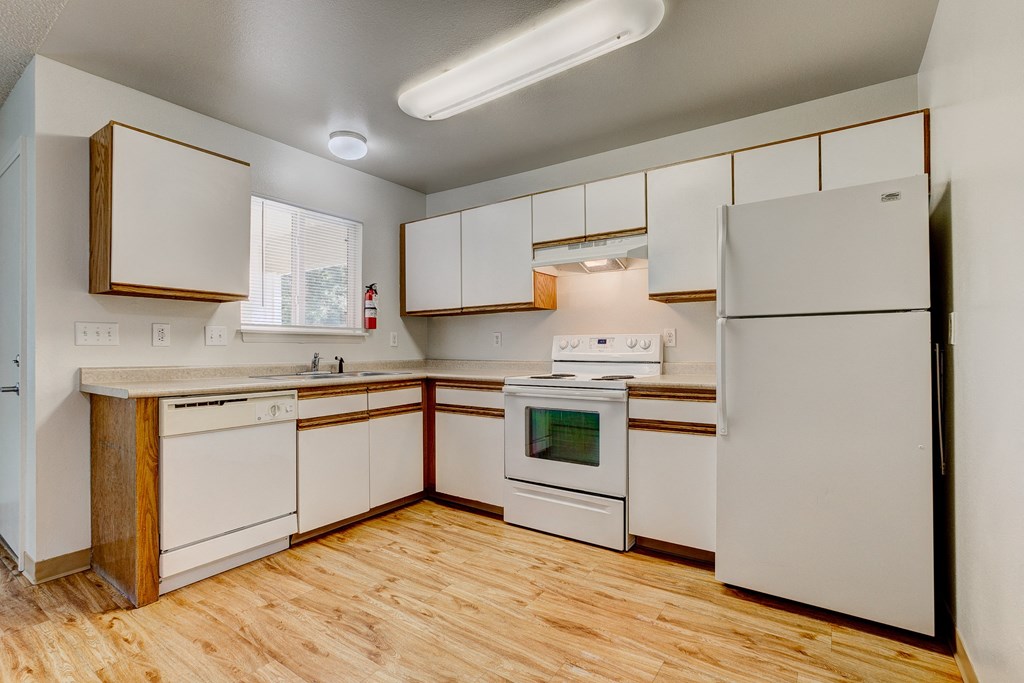 an empty kitchen with white appliances and wood flooring