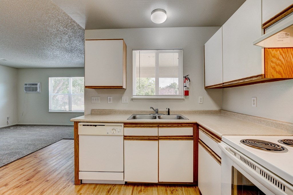 an empty kitchen with white appliances and wooden floors