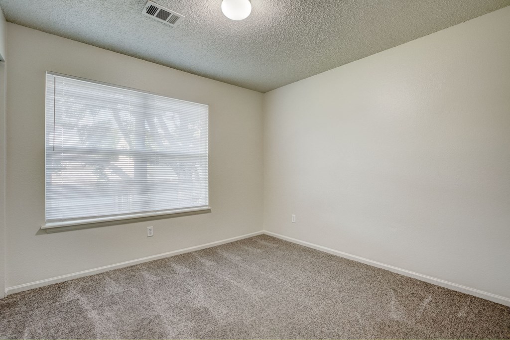 an empty bedroom with a large window and carpeting
