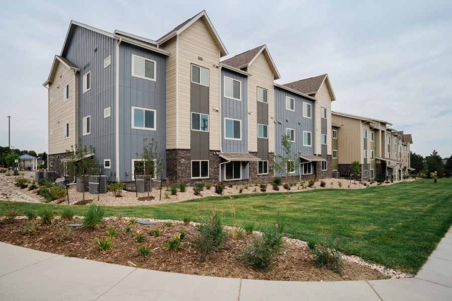 A row of modern townhouses with a sidewalk in front.
