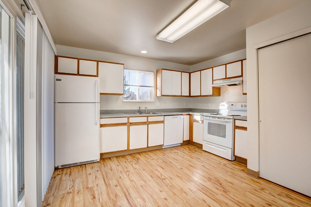 A kitchen with white appliances and wooden floors.