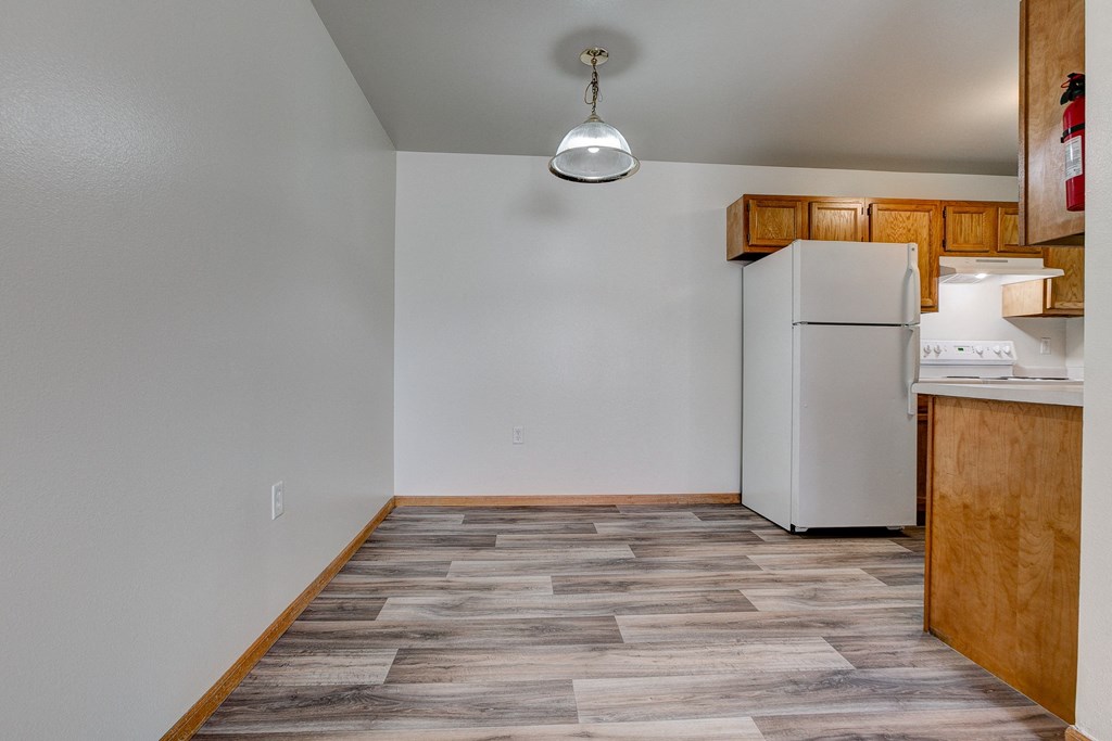 an empty living room with a kitchen with a refrigerator