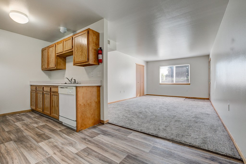 the living room and kitchen of an empty house with wood flooring and a window