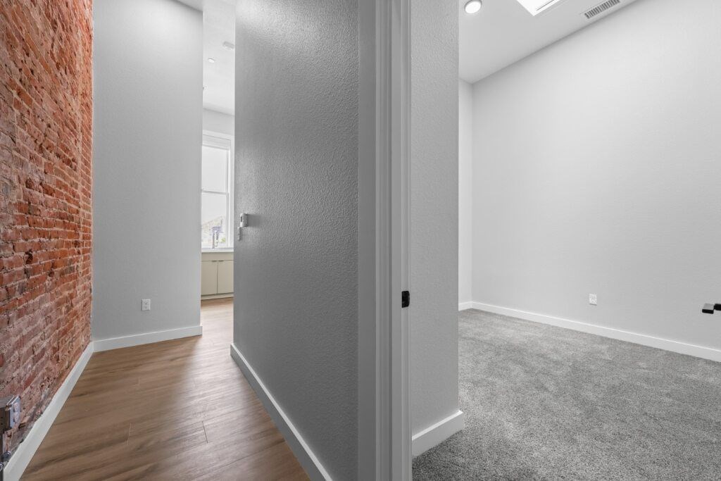 A room with a grey door and a brick wall on the left side at The Avenue Lofts Golden Apartments, Colorado