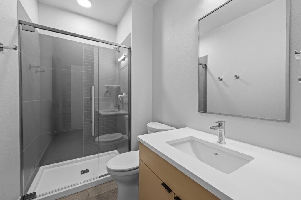 A modern bathroom with a walk-in shower, toilet, and sink at The Avenue Lofts Golden Apartments, Golden, CO, 80401