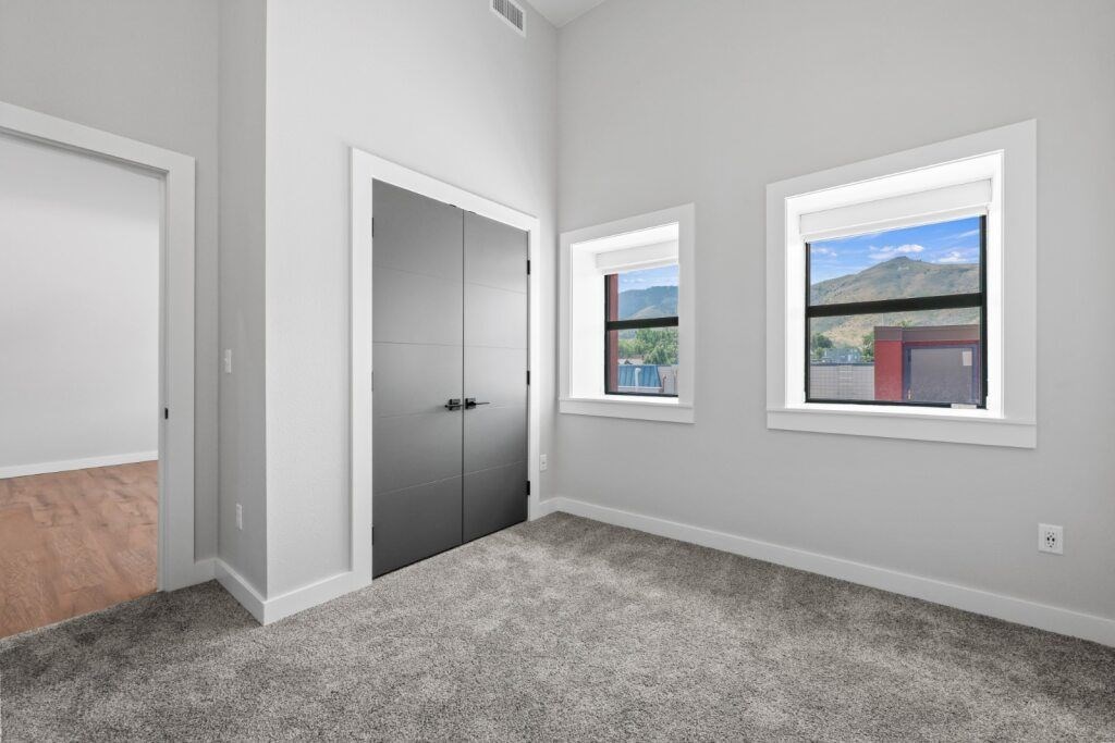A room with a grey carpet, a white door, a grey wardrobe and a window with a view of the mountains at The Avenue Lofts Golden Apartments, Golden, CO