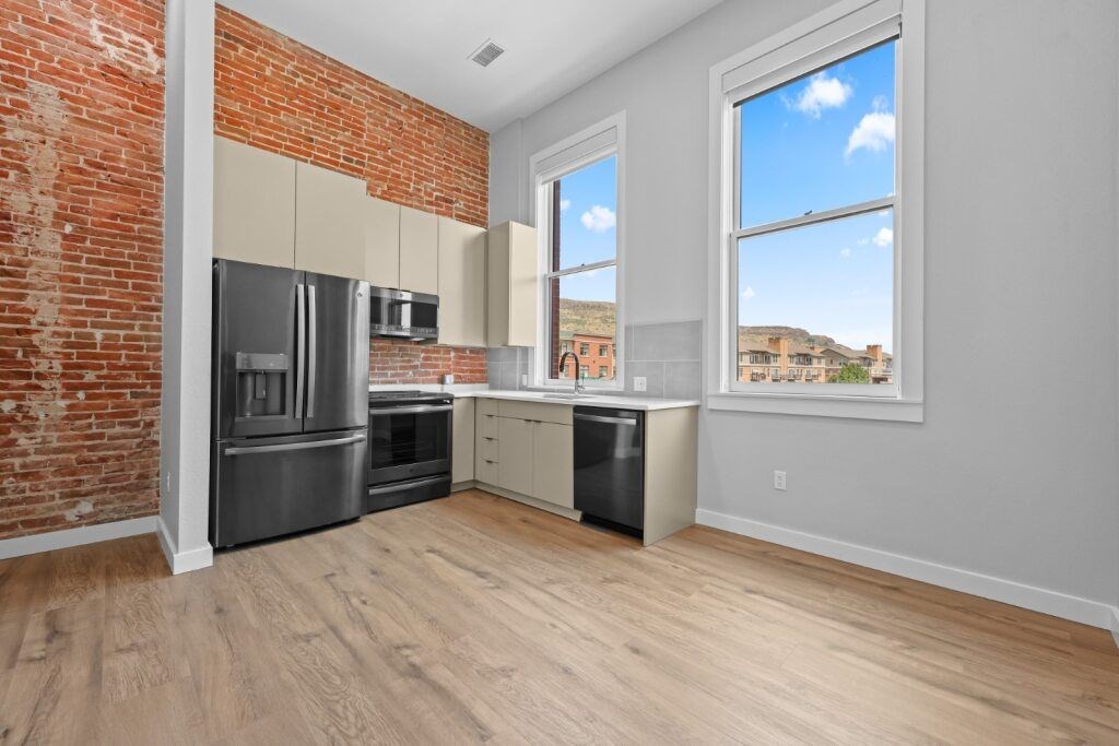 A kitchen with a brick wall and wooden floors at The Avenue Lofts Golden Apartments, Golden, CO