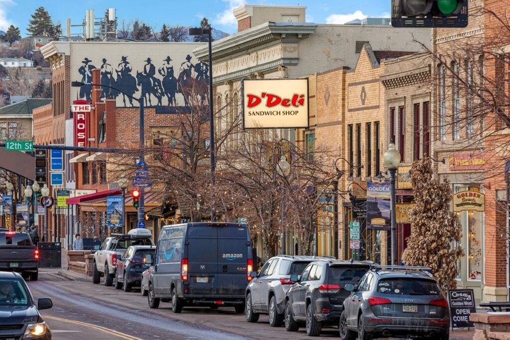 Cars are parked on the side of a street in front of a deli at The Avenue Lofts Golden Apartments, Golden, CO