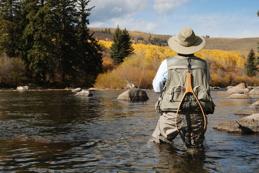 A man in a hat and waders stands in a river holding a fly fishing net at The Avenue Lofts Golden Apartments, Golden, CO, 80401