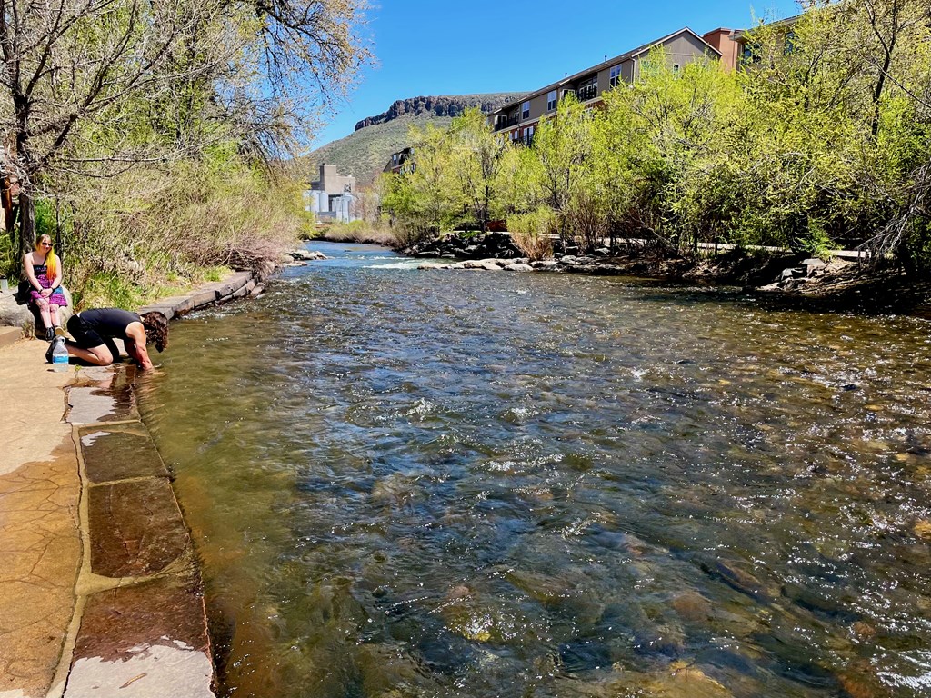 A river flows through a natural landscape with people enjoying the water at The Avenue Lofts Golden Apartments, Golden, CO