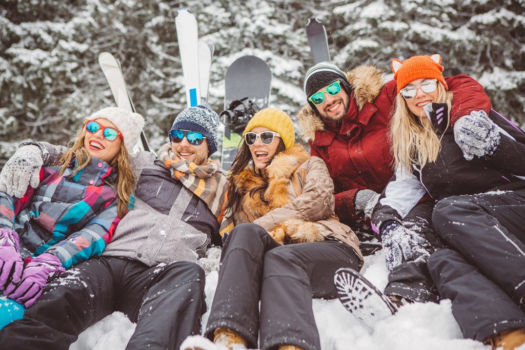A group of friends are sitting in the snow with their skis and snowboards at The Avenue Lofts Golden Apartments, Golden, CO