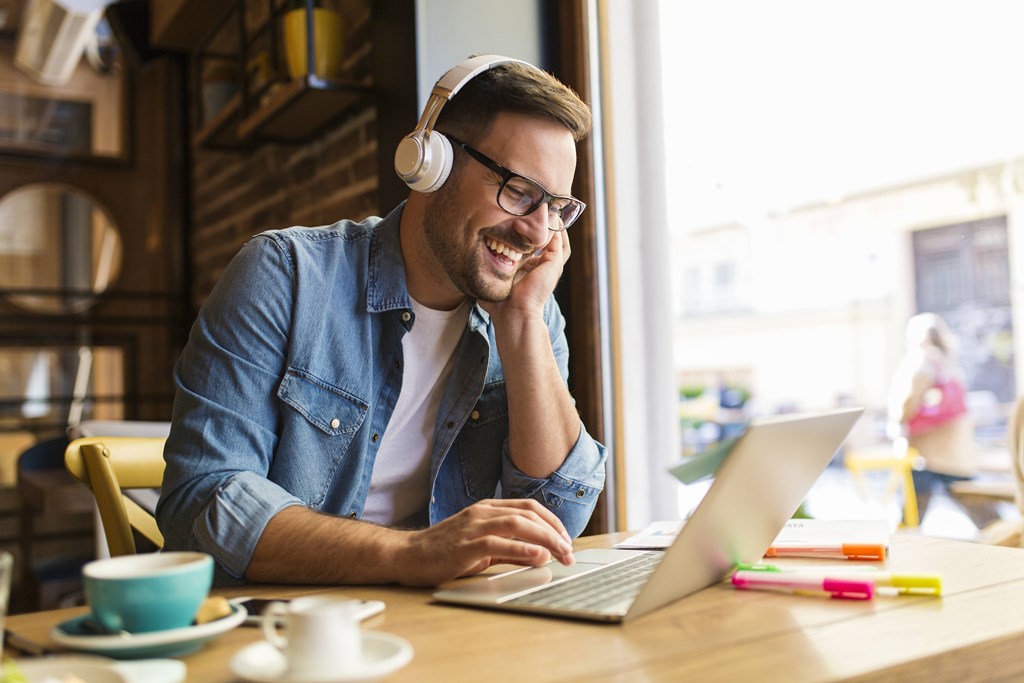 A man in a denim shirt is using a laptop and wearing headphones at The Avenue Lofts Golden Apartments, Golden 80401
