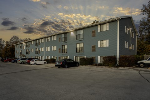 A parking lot in front of a grey apartment building with cars parked.