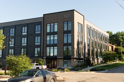 A grey car is parked in front of a building with the number 1601 on it.
