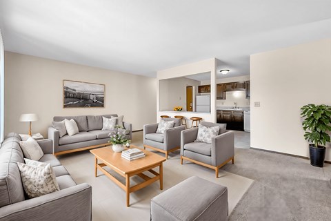 A living room with a grey couch, a grey armchair, a grey ottoman, a wooden coffee table, a potted plant, and a framed picture on the wall.
