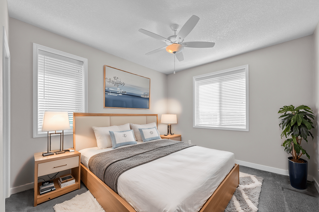 A bedroom with a bed, two lamps, a ceiling fan, and a potted plant.