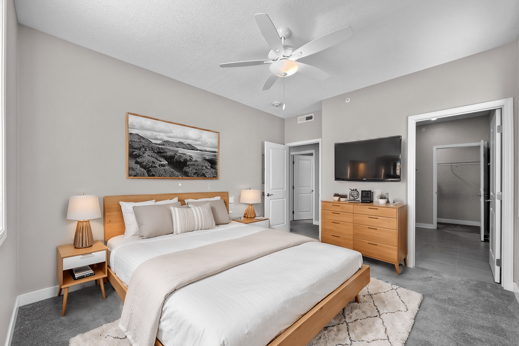 A bedroom with a large bed, a ceiling fan, and a painting on the wall.