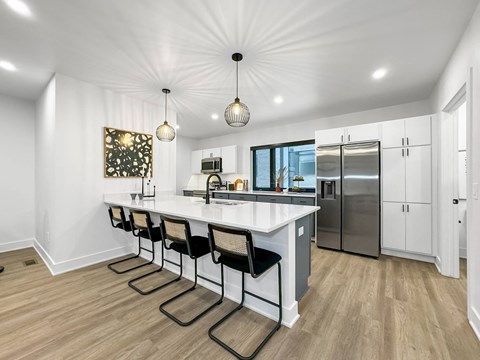a white kitchen with a large island and a stainless steel refrigerator