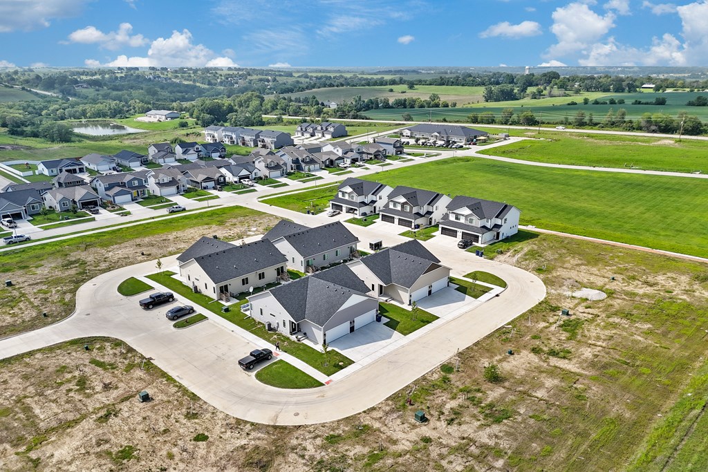 A large, modern house with a driveway and several cars is surrounded by smaller houses in a rural setting.