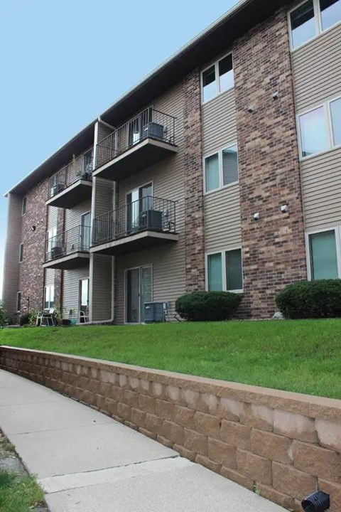 A brick apartment building with balconies and green bushes in front.