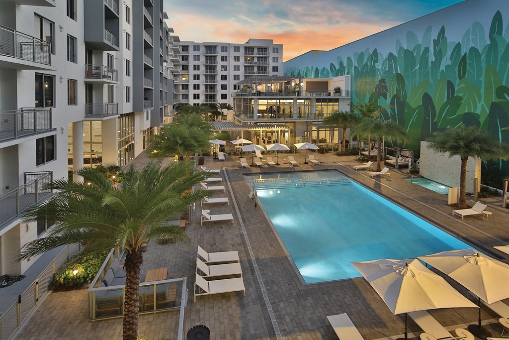 Resort style pool within the community, with balconies overlooking it, a large nature inspired mural, a marble waterfall at the spa, cabanas, palm trees scattered around, and white pool lounge chairs.