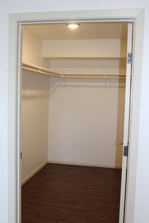 A white door is open to a large closet with a wooden floor and a white wall.
