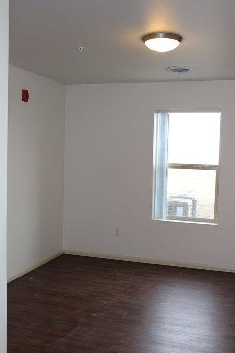 A room with a window and a fire alarm on the wall.