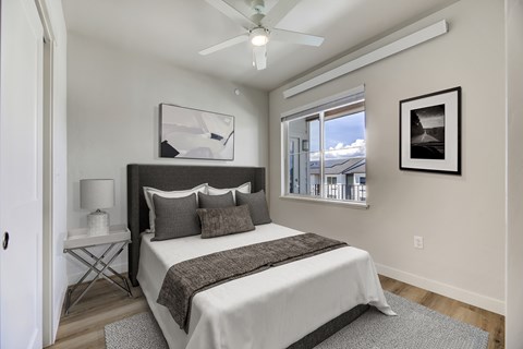 A bedroom with a bed, a ceiling fan, and a window overlooking a snowy landscape.