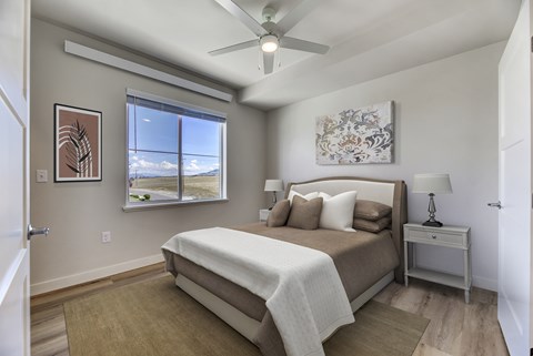 A bedroom with a large bed, a ceiling fan, and a window with a view of the sky.