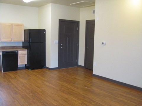 A black refrigerator in a kitchen with wooden floors and cabinets.