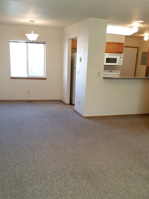 an empty living room with a kitchen and a window