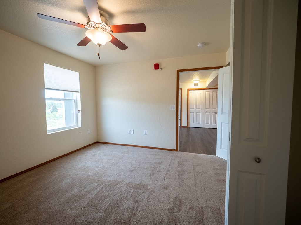 Image of a carpeted bedroom with overhead fan and window