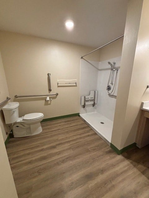A white toilet is in a small bathroom with wood flooring.