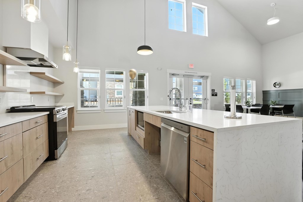 A modern community room with kitchen with a large island and stainless steel appliances.