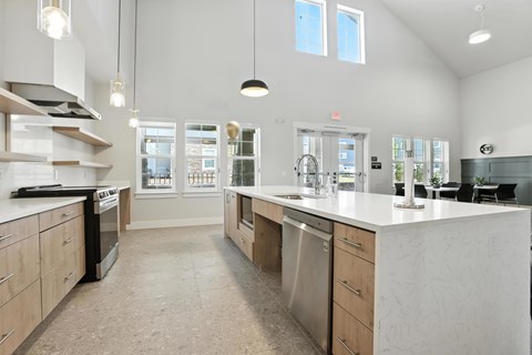 A modern community room with kitchen with a large island and stainless steel appliances.