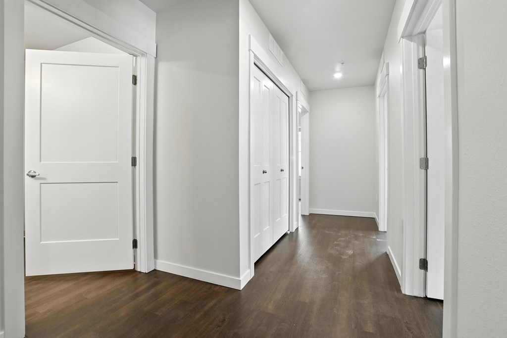 A hallway with white doors and wood floors.