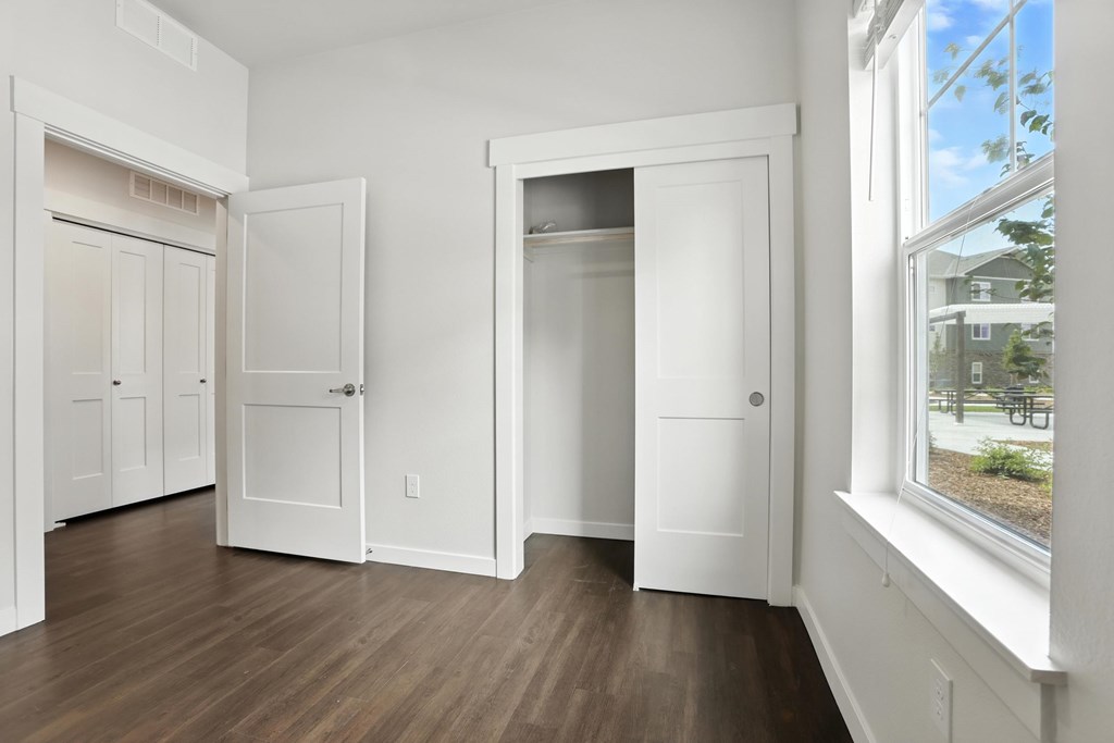 A room with white walls and wooden floors has three white doors.