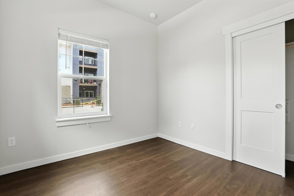 A room with a white door and a window showing a building outside.